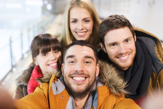 people, friendship, technology and leisure concept - happy friends taking selfie with camera or smartphone on skating rink