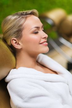 people, beauty, healthy lifestyle and relaxation concept - close up of beautiful young woman resting on chair in bath robe at spa