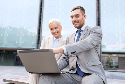 business, education, technology and people concept - smiling businesspeople working with laptop computer on city street