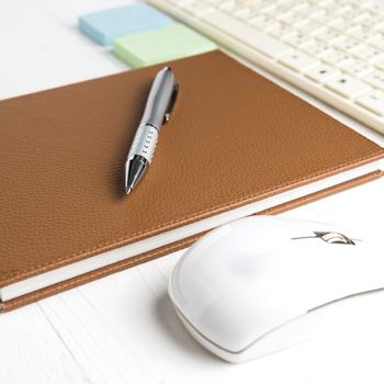 computer and brown notebook with office supplies on white table