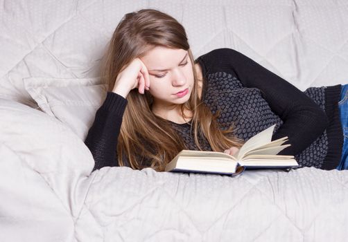 Beautiful young blond woman reading book on the bed at home