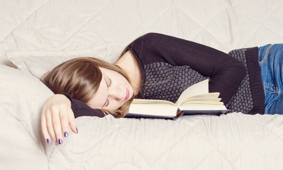 Cute girl sleeping while holding a book lying on her bed