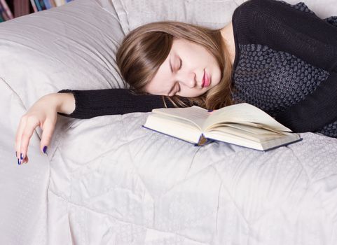 Cute girl sleeping while holding a book lying on her bed
