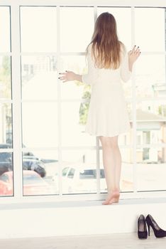 Beautiful young woman is looking out the window 