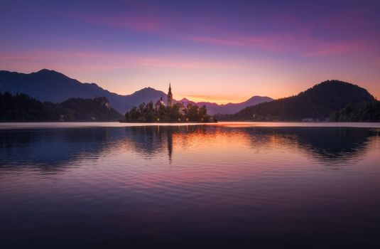 Little Island with Catholic Church in Bled Lake, Slovenia  at Sunrise with Castle and Mountains in Background
