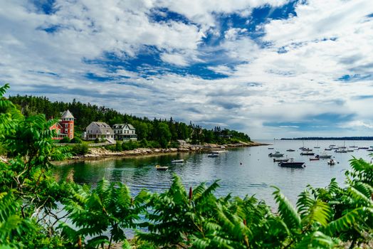 Under a brilliant blue New England sky, boats swing at their moorings in a quiet New England cove.