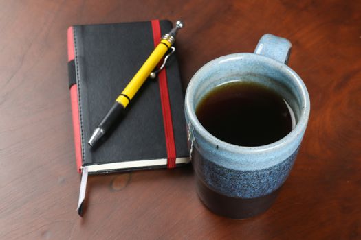 blue design mug of tea and coffee on wood table with notebook and pen