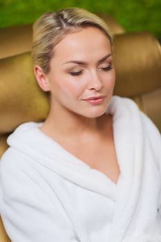 people, beauty, healthy lifestyle and relaxation concept - close up of beautiful young woman resting on chair in bath robe at spa