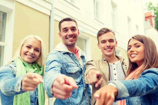 travel, vacation and friendship concept - group of smiling friends in city pointing finger at you