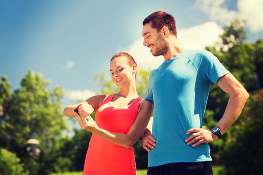 fitness, sport, training, technology and lifestyle concept - two smiling people with heart rate watches outdoors