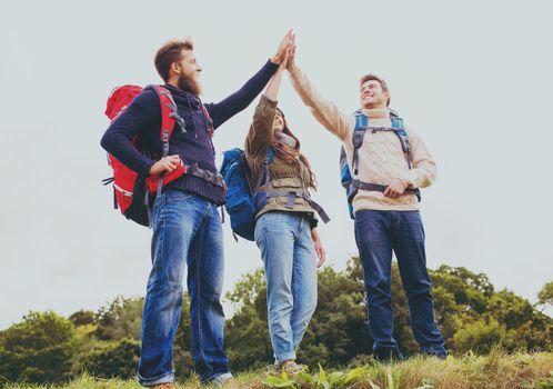 travel, tourism, hike, gesture and people concept - group of smiling friends with backpacks making high five outdoors