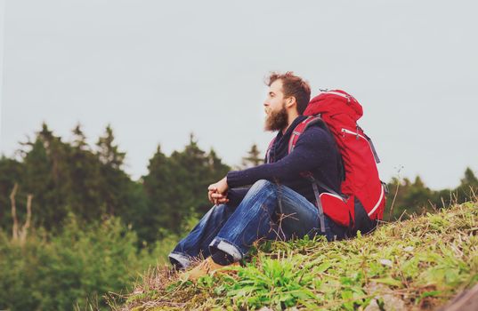 adventure, travel, tourism, hike and people concept - man with beard and red backpack sitting on ground