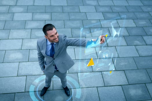 business, development, technology and people and concept - young smiling businessman pointing finger to virtual screens with graphs outdoors from top