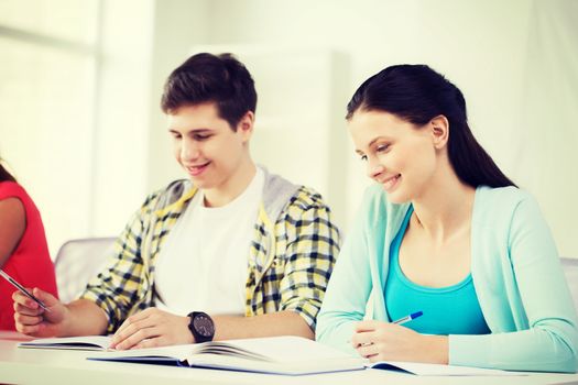 education and school concept - two smiling students with textbooks and books at school