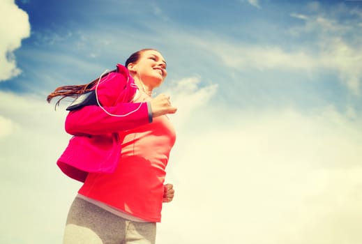 fitness, sport and lifestyle concept - smiling young woman with earphones running outdoors