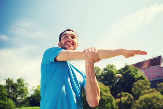 fitness, sport, training and lifestyle concept - smiling man stretching hand outdoors