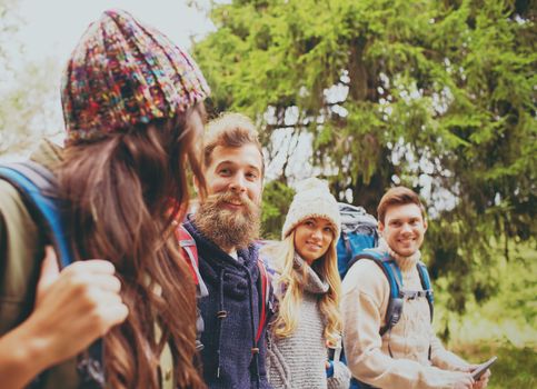 adventure, travel, tourism, hike and people concept - group of smiling friends with backpacks and tablet pc computer walking outdoors