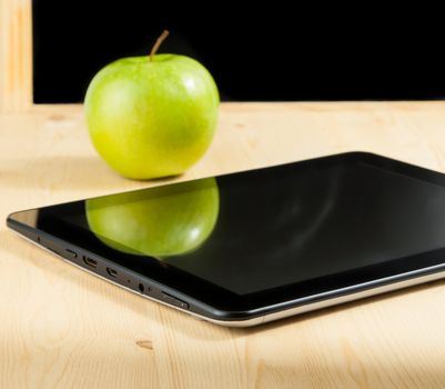 digital tablet pc and green apple in front of blackboard on wood table, concept of learn new technology