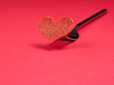 decorative red heart near a fork on red background with space for text, concept valentine day dinner 