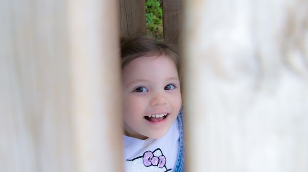 child laughs hidden behind a wooden fence