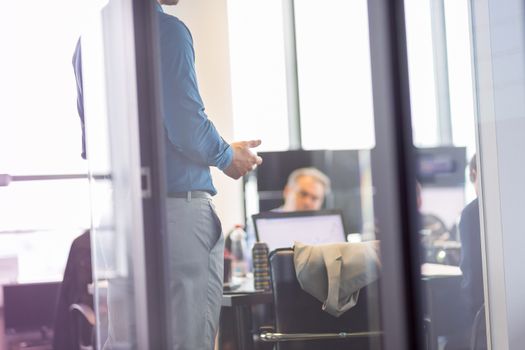 Business man making a presentation at office. Business executive delivering a presentation to his colleagues during meeting or in-house business training. View through glass.