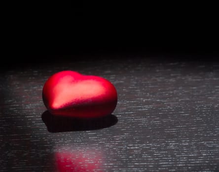 one decorative red heart on black dark light and on wood table with space for text, concept of valentine day