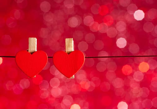 two decorative red hearts hanging against red light bokeh background with space for text, concept of valentine day