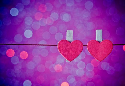 two decorative red hearts hanging against blue and violet light bokeh background with space for text, concept of valentine day