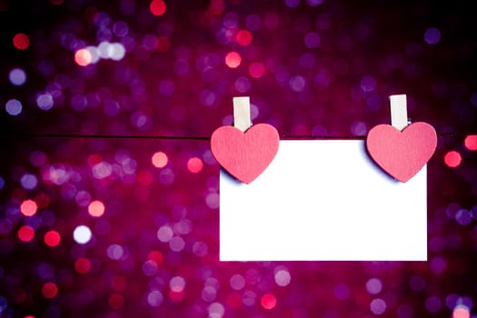 two decorative red hearts with greeting card hanging on blue and violet light bokeh background with space for text, concept of valentine day