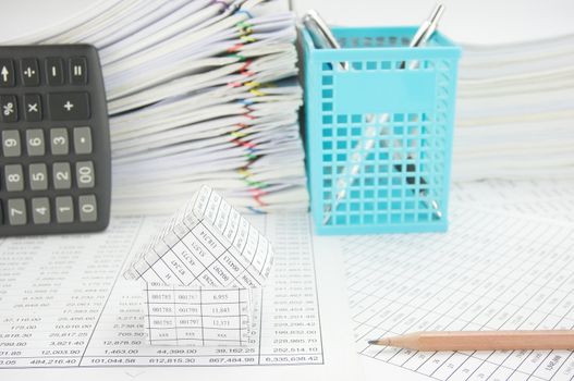 House with pencil on finance account have vertical calculator and blue pen basket with paper of report and paperwork as background.