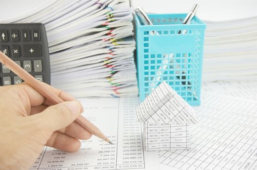 Man holding pencil for audit with house on finance account have vertical calculator and blue pen basket with paper of report and paperwork as background.