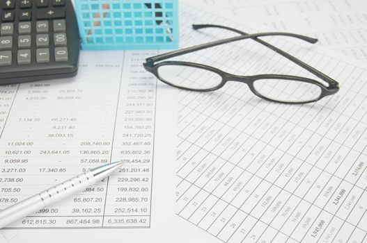 Silver pen have spectacles and calculator with blue pencil basket on finance account as background.