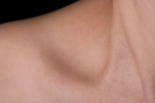 An abstract shot of a woman's neck, collarbone and shoulder with a small amount of black background showing.
