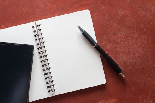 Opened notepad with pen and black smart phone on rustic cement background with low key scene.