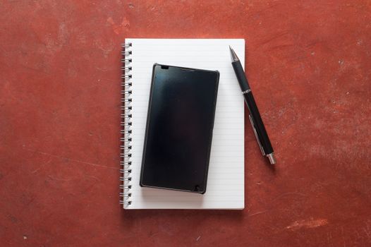 Opened notepad with pen and black smart phone on rustic cement background with low key scene.