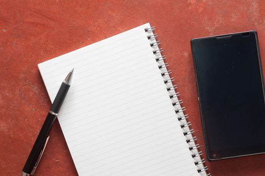 Opened notepad with pen and black smart phone on rustic cement background with low key scene.