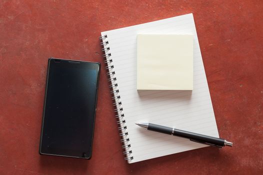 Opened notepad with pen, small sticky paper and black smart phone on rustic cement background with low key scene.