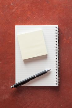 Opened notepad with pen, small sticky paper on rustic cement background with low key scene.