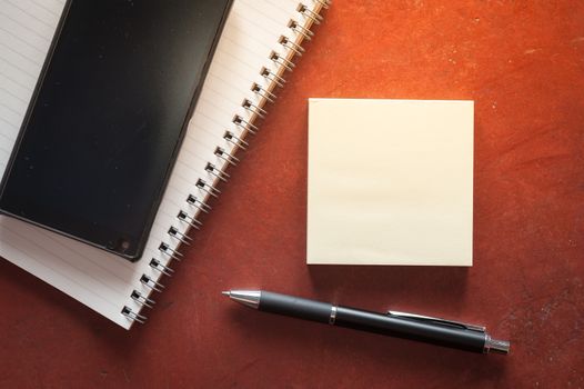Opened notepad with pen, small sticky paper and black smart phone on rustic cement background with low key scene.