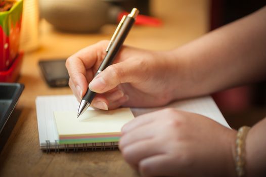 Woman right hand writing on notepad at wood bar in coffee shop with morning scene