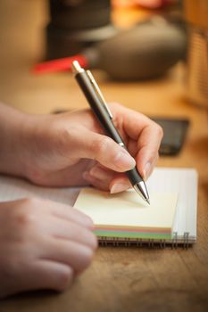Woman left hand writing on notepad at wood bar in coffee shop with morning scene