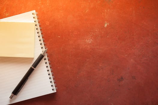 Opened notepad with pen, small sticky paper on red cement background with morning scene