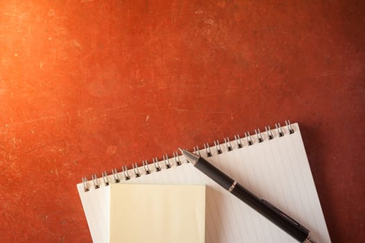 Opened notepad with pen, small sticky paper on red cement background with morning scene
