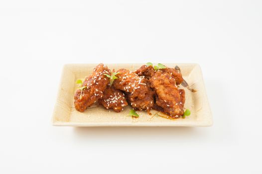Korean fusion style deep fried chicken wings seasoned with Korean spicy kimchi sauce on square ceramic dish