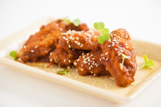 Korean fusion style deep fried chicken wings seasoned with Korean spicy kimchi sauce on square ceramic dish
