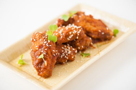 Korean fusion style deep fried chicken wings seasoned with Korean spicy kimchi sauce on square ceramic dish