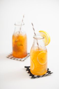 Iced lemon tea garnished with lemon in glass bottle with peppermint toffee tea on background