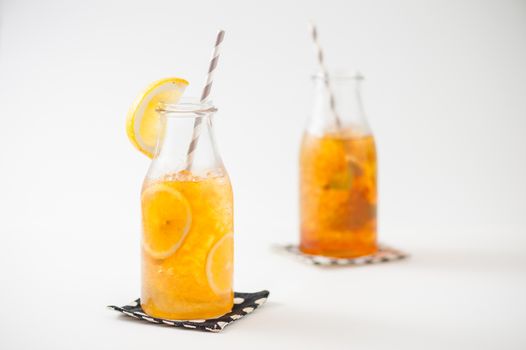 Iced lemon tea garnished with lemon in glass bottle with peppermint toffee tea on background