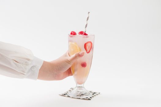 Woman left hand holding glass of iced berry lemonade with striped straw garnished with lemon, raspberry and strawberry