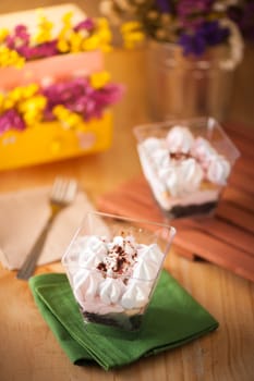 1 banoffee pie in plastic cup on green napkin on wood table with another one in background with afternoon scene